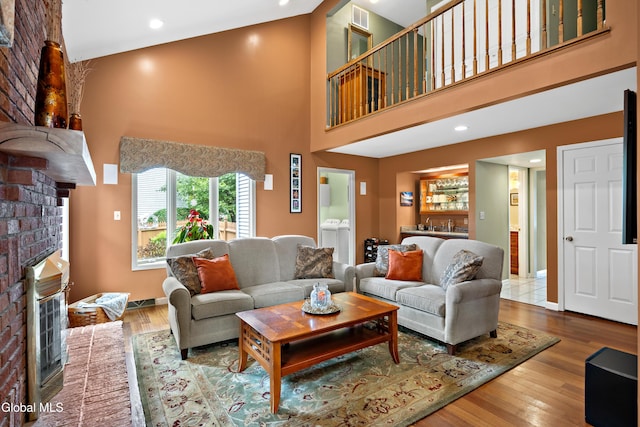 658 Salvia Ln, Guilderland, NY 12303 - living room with a brick fireplace, washing machine and clothes dryer, a high ceiling, wood finished floors, and bar