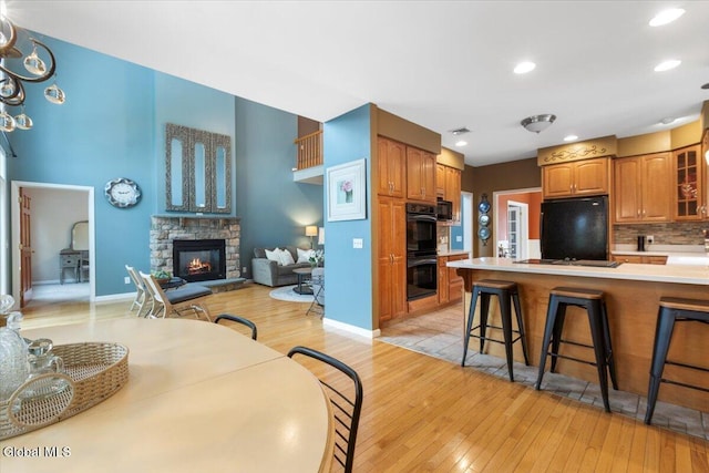 14 Maplecrest Dr, Ravena, NY 12143 - kitchen with black appliances, light wood finished floors, glass insert cabinets, a kitchen bar, and a fireplace