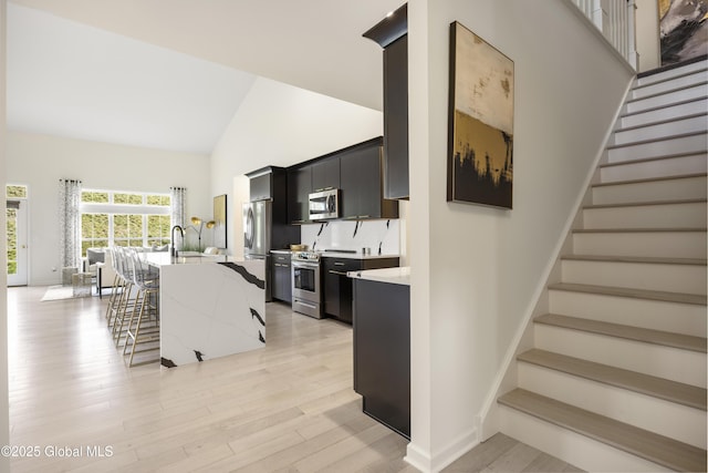 10A Idared Ln, Halfmoon, NY 12065 - kitchen with stainless steel appliances, high vaulted ceiling, dark cabinets, an island with sink, and light wood-style flooring