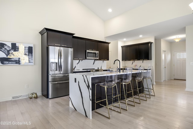 10A Idared Ln, Halfmoon, NY 12065 - kitchen featuring appliances with stainless steel finishes, a kitchen bar, light wood-style flooring, a kitchen island with sink, and high vaulted ceiling