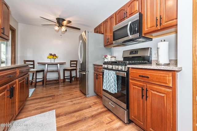 23 Mcmillen Pl, Bethlehem, NY 12054 - kitchen with stainless steel appliances, ceiling fan, light wood-style flooring, brown cabinets, and light stone counters