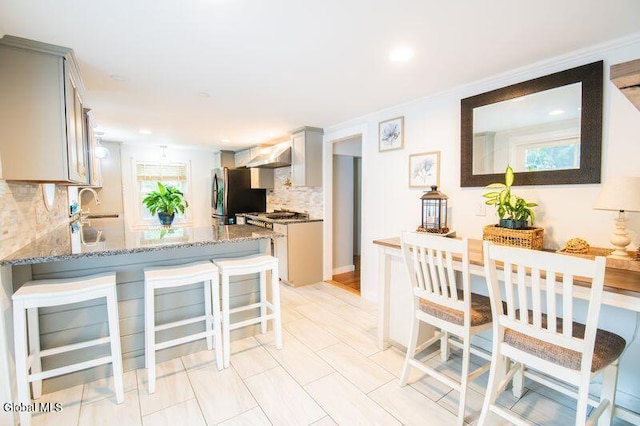 1264 Pilot Knob Rd, Fort Ann, NY 12844 - kitchen with wall chimney exhaust hood, freestanding refrigerator, gray cabinetry, backsplash, and light stone countertops