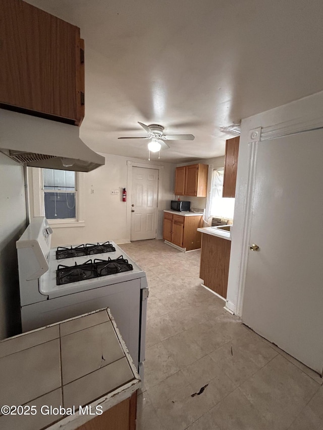 1133 Cutler St, Schenectady, NY 12303 - kitchen with white range with gas cooktop, exhaust hood, brown cabinets, ceiling fan, and light countertops