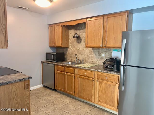 2059 Rosedale Way, Guilderland, NY 12303 - kitchen featuring appliances with stainless steel finishes, tasteful backsplash, light tile patterned flooring, dark countertops, and brown cabinetry
