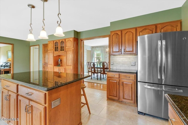 630 Salvia Ln, Guilderland, NY 12303 - kitchen featuring freestanding refrigerator, dark stone countertops, a breakfast bar area, decorative backsplash, and brown cabinets