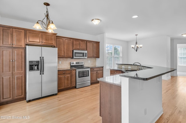 21 Beacon Dr, Colonie, NY 12189 - kitchen with stainless steel appliances, a chandelier, light wood-type flooring, decorative backsplash, and brown cabinetry