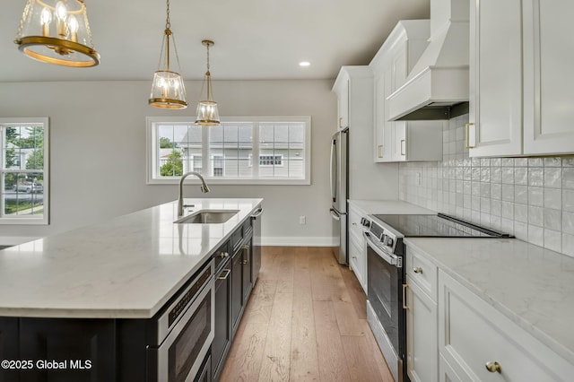606 Vly Pointe Dr, Niskayuna, NY 12309 - kitchen featuring appliances with stainless steel finishes, premium range hood, light wood-style floors, a center island with sink, and white cabinetry