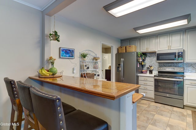 909 Ash Tree Ln, Niskayuna, NY 12309 - kitchen with stainless steel appliances, a kitchen breakfast bar, backsplash, light countertops, and ornamental molding