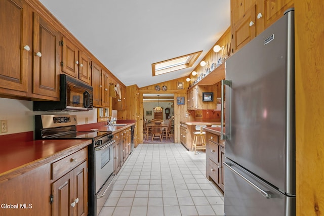 135 Willow St, Guilderland, NY 12084 - kitchen with appliances with stainless steel finishes, vaulted ceiling, a skylight, light tile patterned floors, and brown cabinets