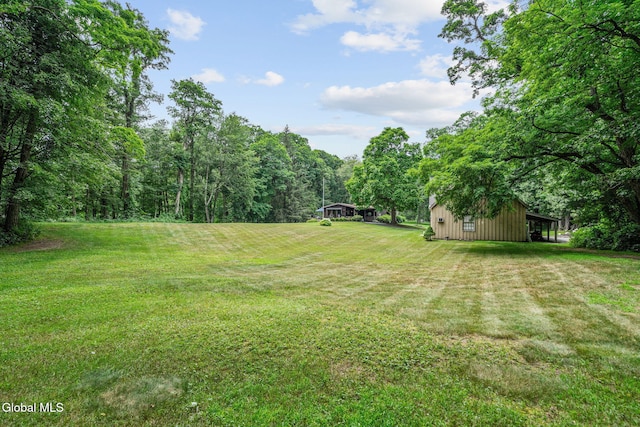 135 Willow St, Guilderland, NY 12084 - view of grassy yard featuring an outbuilding, a wooded view, and a carport