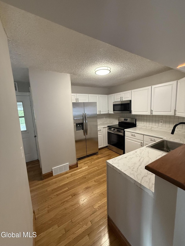5 Crowsnest Ct, Halfmoon, NY 12188 - kitchen with stainless steel appliances, light wood-style floors, white cabinetry, a textured ceiling, and decorative backsplash