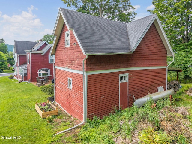 138 Elm St, Cobleskill, NY 12043 - view of property exterior featuring a lawn, roof with shingles, a patio area, and a garden