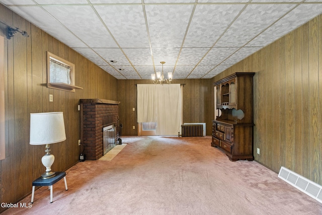 2780 Campbell Ave, Schenectady, NY 12306 - unfurnished living room featuring radiator, carpet floors, wooden walls, a brick fireplace, and a chandelier