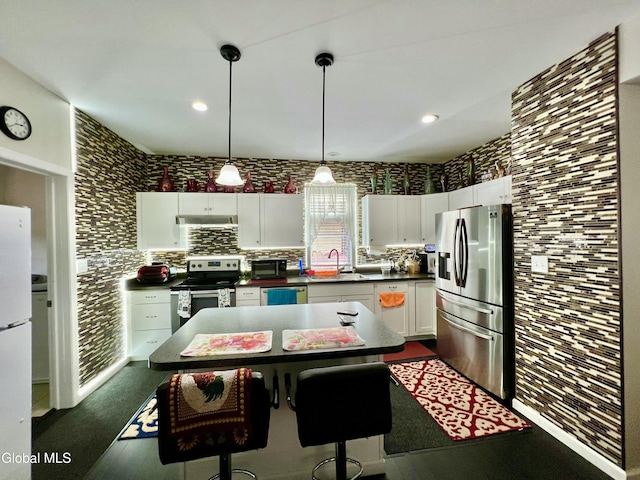 101 Prospect St, Schenectady, NY 12308 - kitchen featuring stainless steel appliances, under cabinet range hood, dark countertops, white cabinetry, and hanging light fixtures