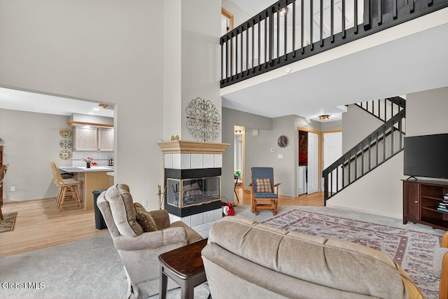 3 Pine Ridge Rd, Saratoga Springs, NY 12866 - living area featuring a tile fireplace, a towering ceiling, stairway, and light wood-style flooring