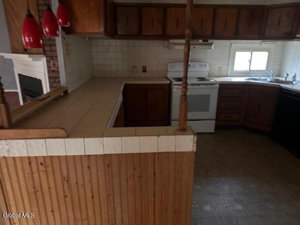 873 W Fulton Rd, Fulton, NY 12187 - kitchen featuring white range with electric cooktop, tile counters, dishwashing machine, ventilation hood, and a fireplace
