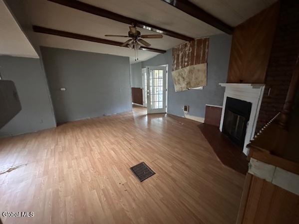 873 W Fulton Rd, Fulton, NY 12187 - unfurnished living room featuring a ceiling fan, a glass covered fireplace, wood finished floors, and beamed ceiling