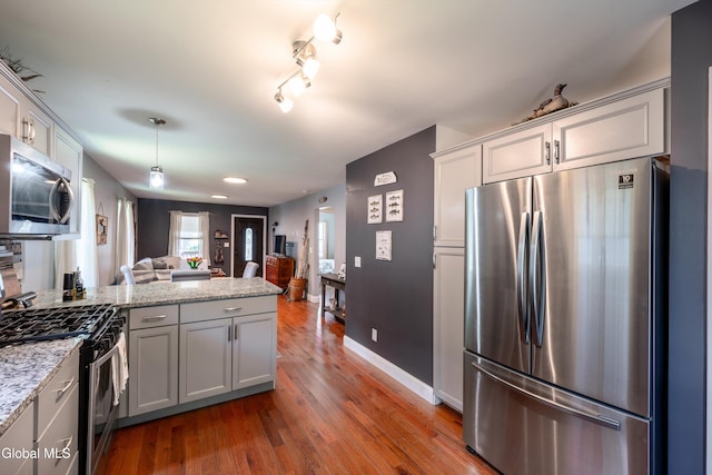 10 3rd St, South Glens Falls, NY 12803 - kitchen featuring stainless steel appliances, a peninsula, open floor plan, wood finished floors, and light stone counters