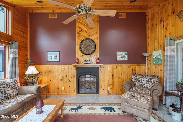 271 Settles Mountain Rd, Cobleskill, NY 12043 - tiled living room featuring wood walls, wooden ceiling, a fireplace, a ceiling fan, and wainscoting