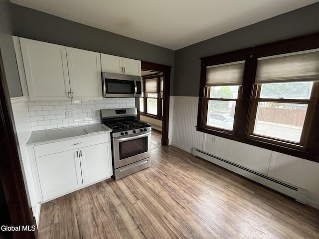 1822 7th St, Rensselaer, NY 12144 - kitchen with stainless steel appliances, a baseboard radiator, light wood-style floors, white cabinets, and a wainscoted wall