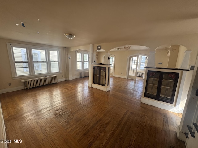 261 Altamont Ave, Schenectady, NY 12304 - unfurnished living room with arched walkways, radiator heating unit, decorative columns, and plenty of natural light
