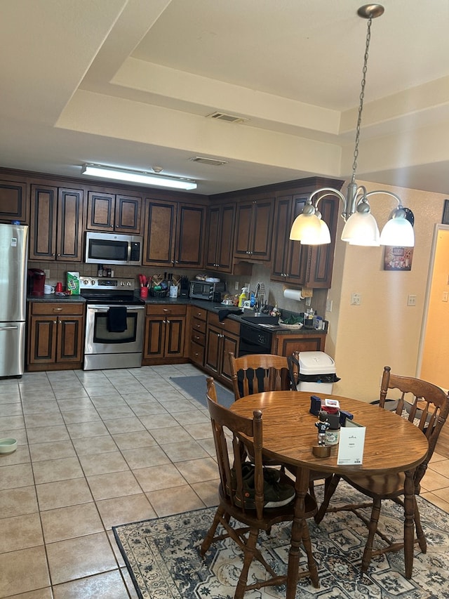 5175 Calvary Cir, Valdosta, GA 31605 - kitchen featuring stainless steel appliances, dark countertops, light tile patterned floors, dark brown cabinets, and a tray ceiling