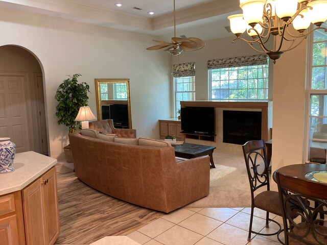 living room with ceiling fan with notable chandelier, light wood-type flooring, crown molding, and a tray ceiling