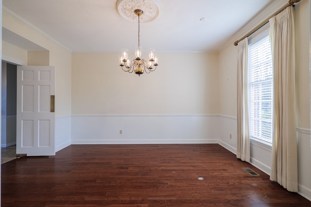 empty room with dark hardwood / wood-style floors, crown molding, a wealth of natural light, and a chandelier