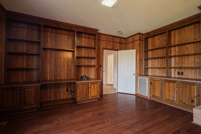 unfurnished office with a textured ceiling, wood walls, and dark wood-type flooring