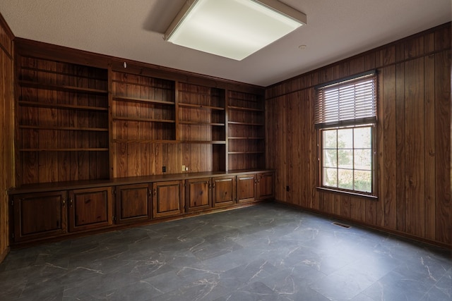 empty room with built in shelves, wood walls, and a textured ceiling