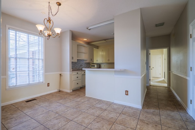 kitchen featuring backsplash, light tile patterned floors, decorative light fixtures, kitchen peninsula, and a chandelier