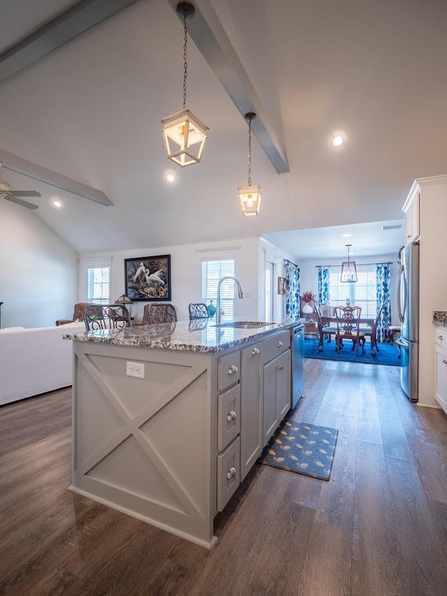 kitchen with lofted ceiling with beams, stainless steel appliances, dark wood-type flooring, a sink, and an island with sink