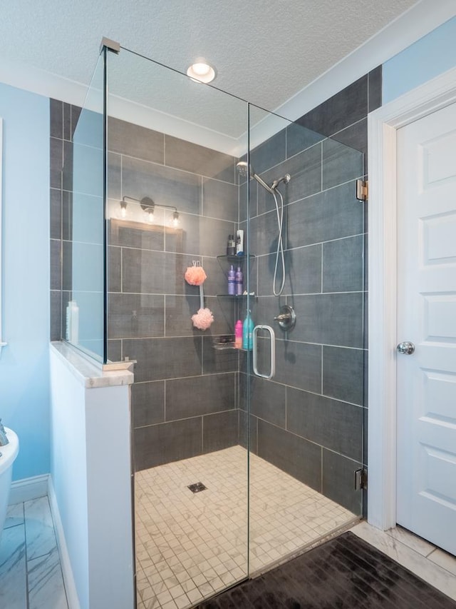 full bath featuring a textured ceiling, marble finish floor, a shower stall, and baseboards