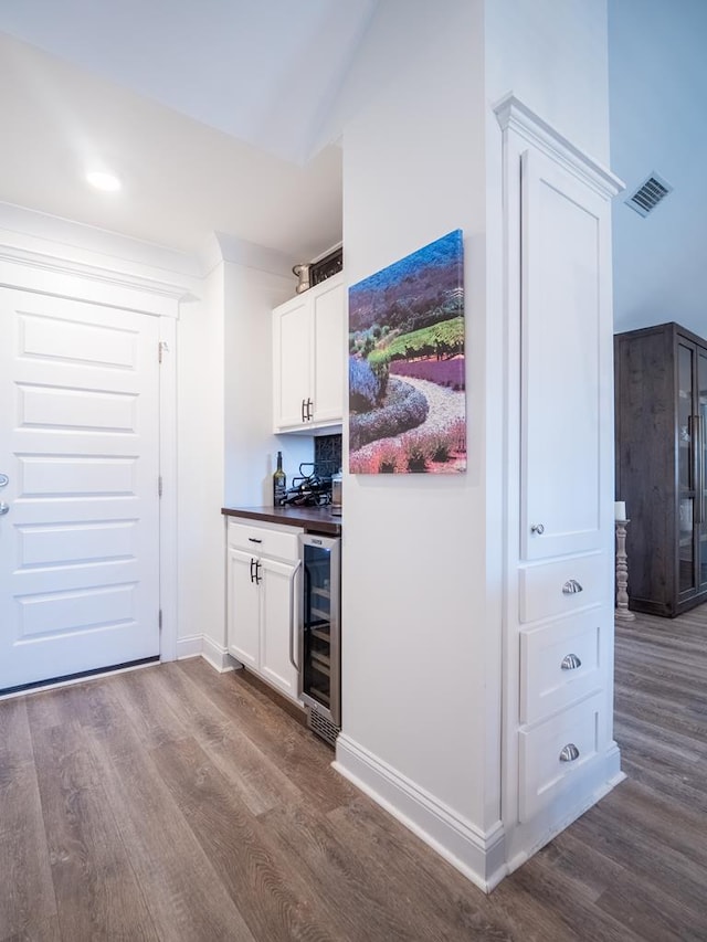 bar with dark wood finished floors, visible vents, a bar, beverage cooler, and baseboards