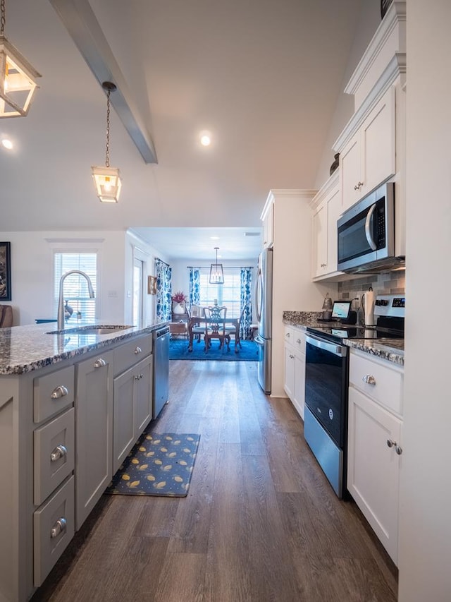 kitchen with light stone counters, a sink, appliances with stainless steel finishes, dark wood finished floors, and decorative light fixtures