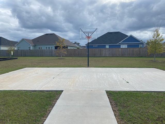 view of basketball court with a lawn and fence