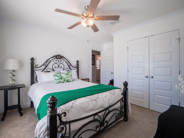 carpeted bedroom featuring a ceiling fan, visible vents, a closet, and ornamental molding