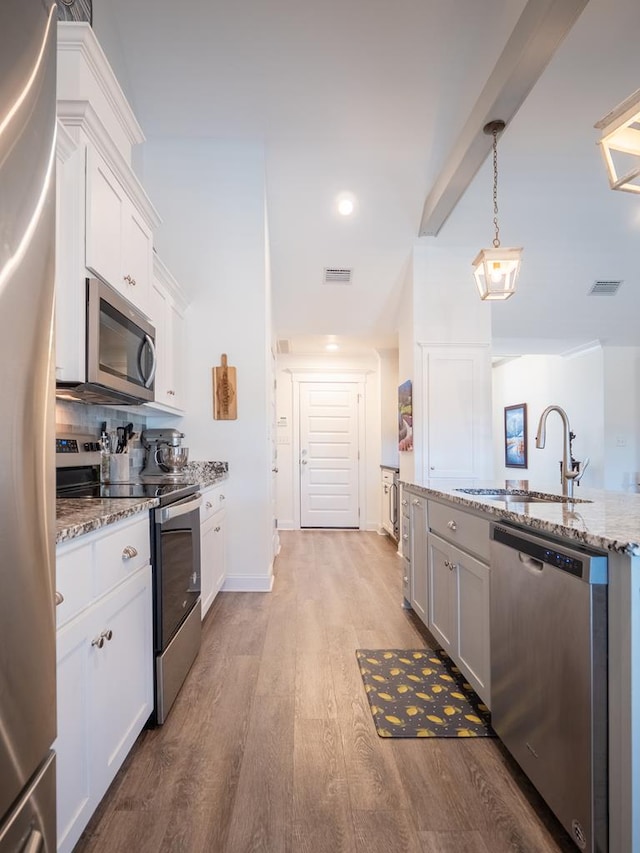 kitchen featuring appliances with stainless steel finishes, light stone counters, light wood-style floors, white cabinetry, and a sink