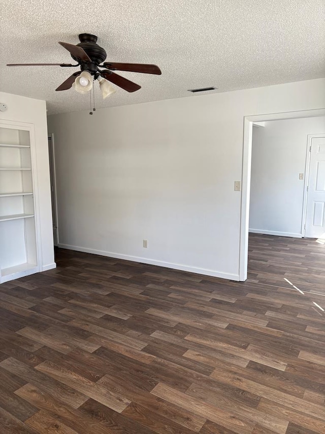 unfurnished room with a textured ceiling, dark wood-type flooring, ceiling fan, and built in shelves