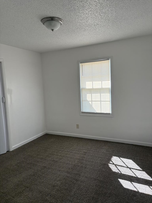 spare room featuring dark carpet and a textured ceiling