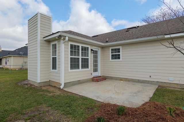 back of property with entry steps, a shingled roof, a lawn, a chimney, and a patio area