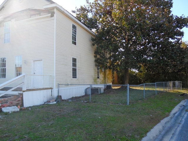 view of property exterior with a lawn, central AC unit, and fence