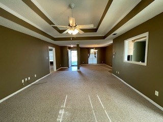 carpeted empty room featuring baseboards, a raised ceiling, and ceiling fan