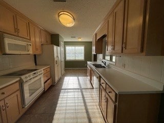 kitchen with a sink, white appliances, light countertops, a textured ceiling, and backsplash