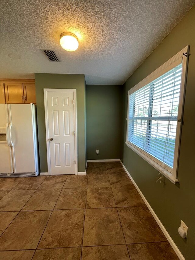 4331 Summerlin Dr, Valdosta, GA 31605 - unfurnished bedroom with a textured ceiling, visible vents, tile patterned floors, baseboards, and white fridge with ice dispenser
