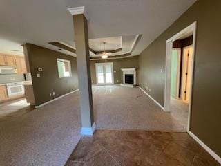 unfurnished living room with a fireplace, baseboards, dark colored carpet, ceiling fan, and a raised ceiling