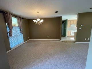 unfurnished room featuring baseboards, carpet flooring, a notable chandelier, and visible vents