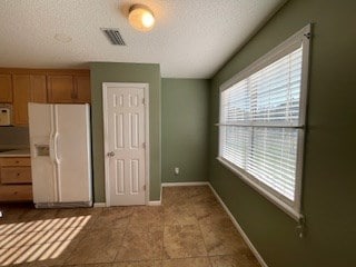 unfurnished bedroom featuring a textured ceiling, visible vents, baseboards, a closet, and white fridge with ice dispenser
