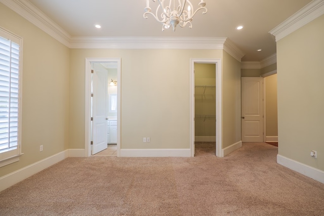 unfurnished bedroom with light carpet, ensuite bathroom, ornamental molding, a spacious closet, and a chandelier