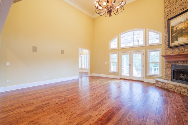 unfurnished living room featuring a high ceiling, ornamental molding, a fireplace, a notable chandelier, and wood-type flooring